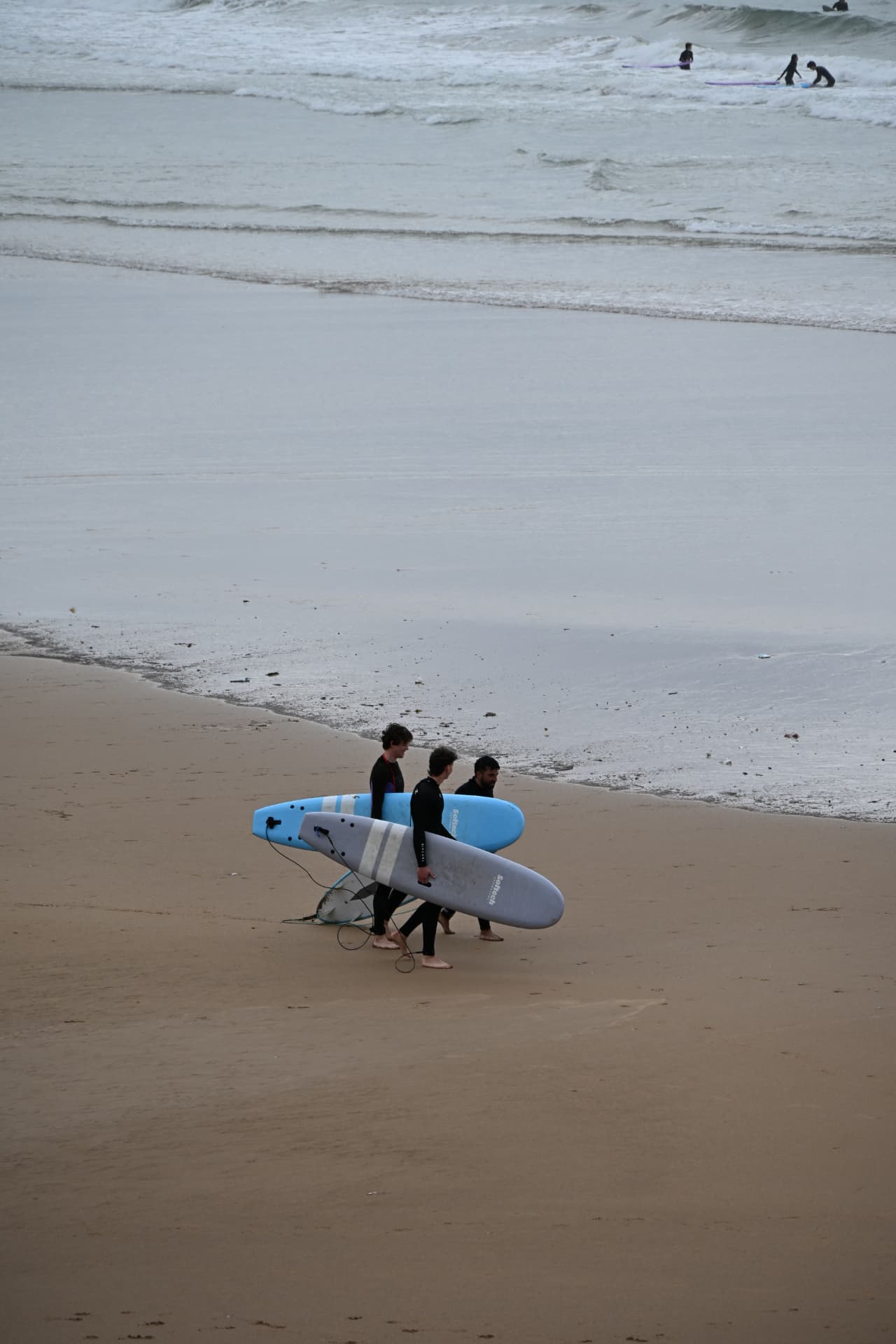 Surfers lopen met hun boards over het strand